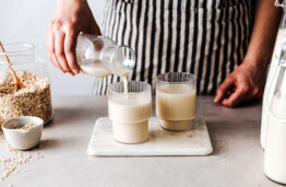 Close-up of a female pouring freshly made oat milk in glasses. Woman serving healthy oat milk.